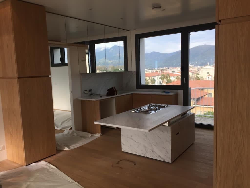 La cucina finita: due colonne in rovere ai lati dell'isola in marmo e la vetrata sulle montagne