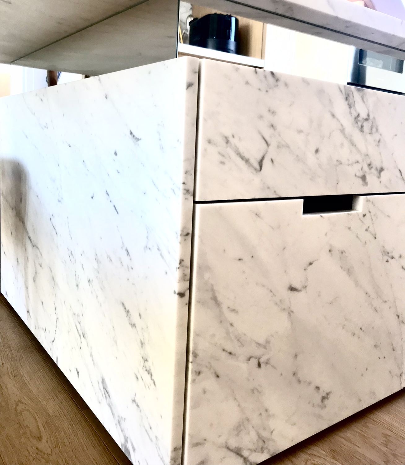 Febbraio 2022: dettaglio dell'isola di cucina in marmo di Carrara, con una fascia a specchio sotto il piano a sbalzo che riflette i mobili in rovere e fa sembrare il blocco di marmo staccato da terra