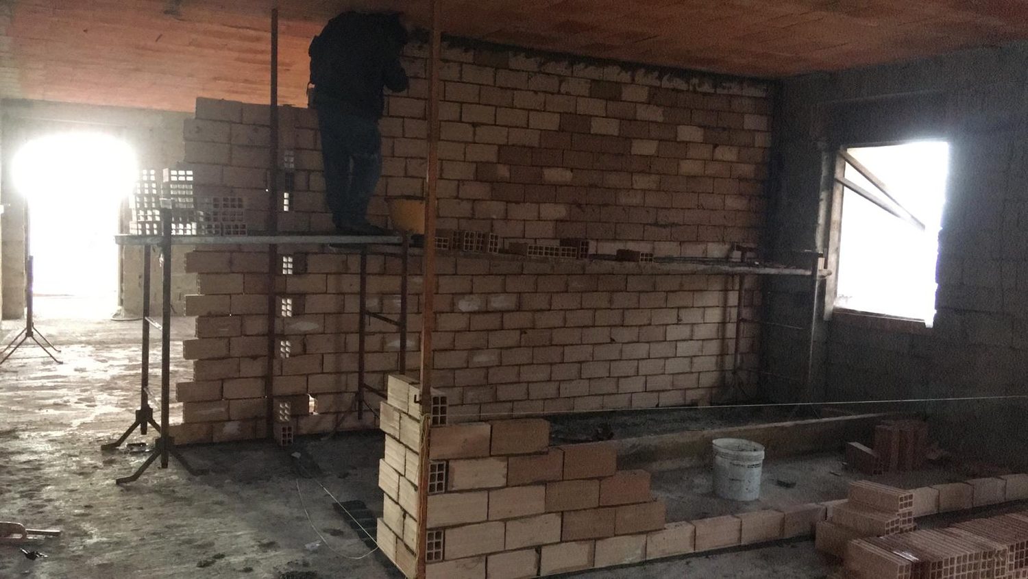 Fotografia di cantiere: il muratore sul trabattello costruisce un tramezzo in laterizio dentro il vano vuoto