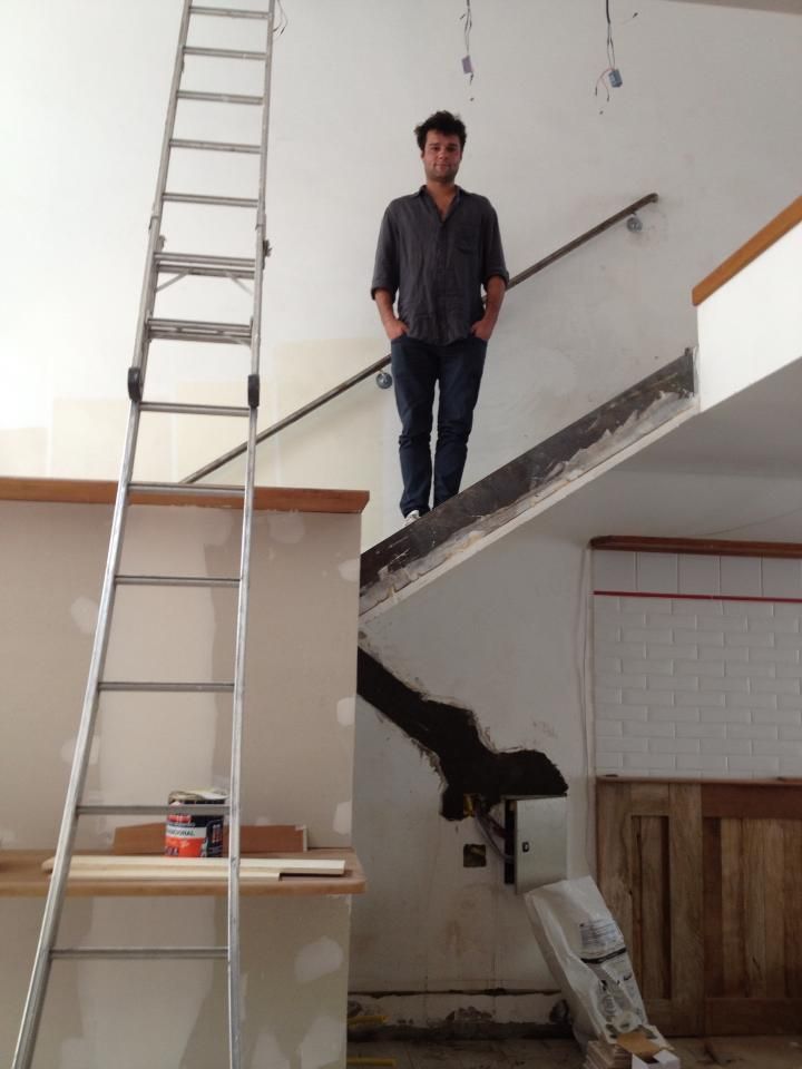 Fotografia di cantiere: Matteo Gardino in piedi sulla scala nuova, ancora senza finiture, con la scala a pioli appoggiata al vuoto a doppia altezza