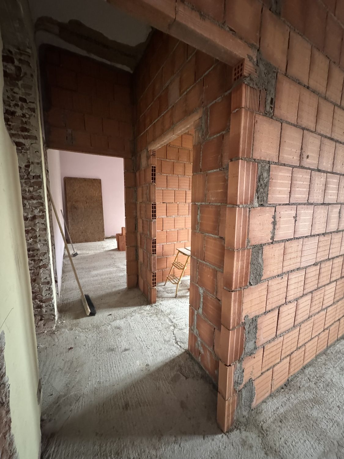 Cantiere: un varco aperto in un muro portante, con il mattone pieno a vista e il pavimento scrostato