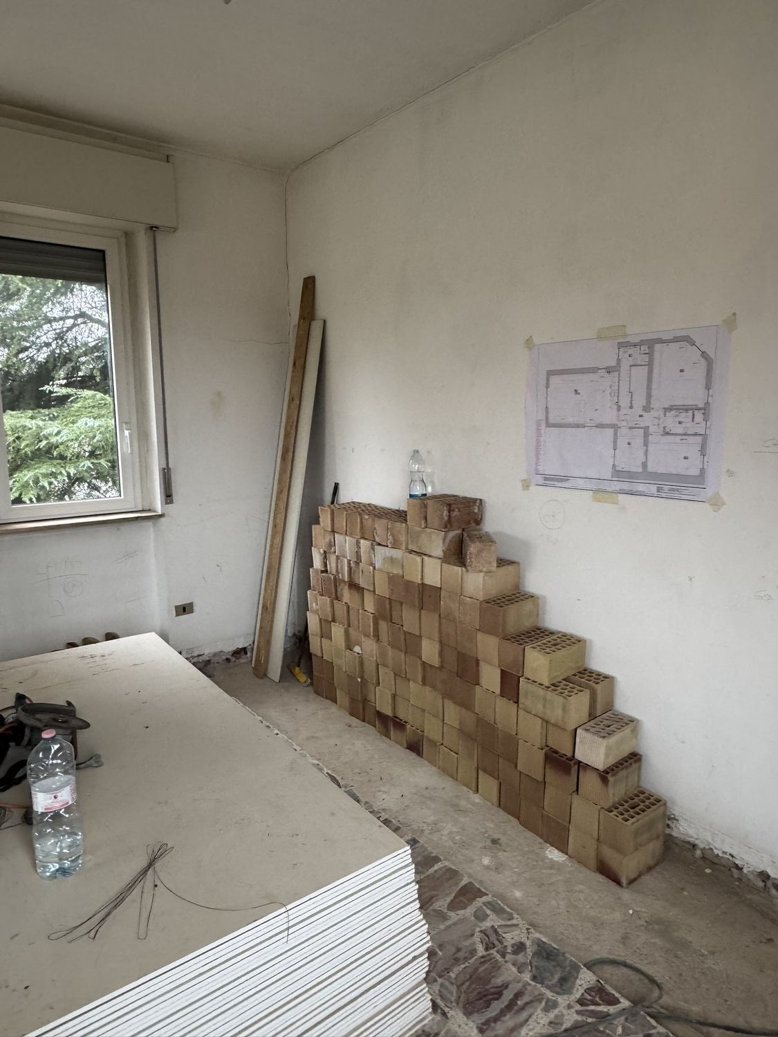 Cantiere: la pianta di progetto stampata e attaccata al muro, accanto ai materiali accatastati