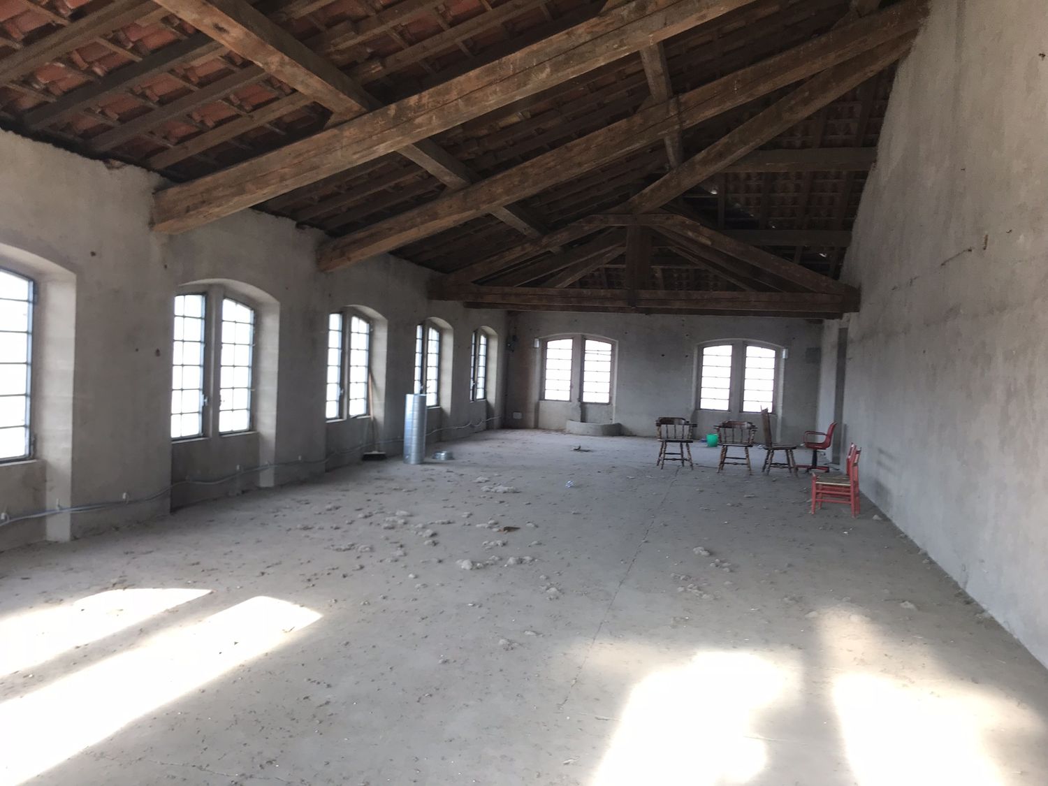 L'interno prima: una sala vuota al piano alto, con il tetto a capriate e le finestre in fila