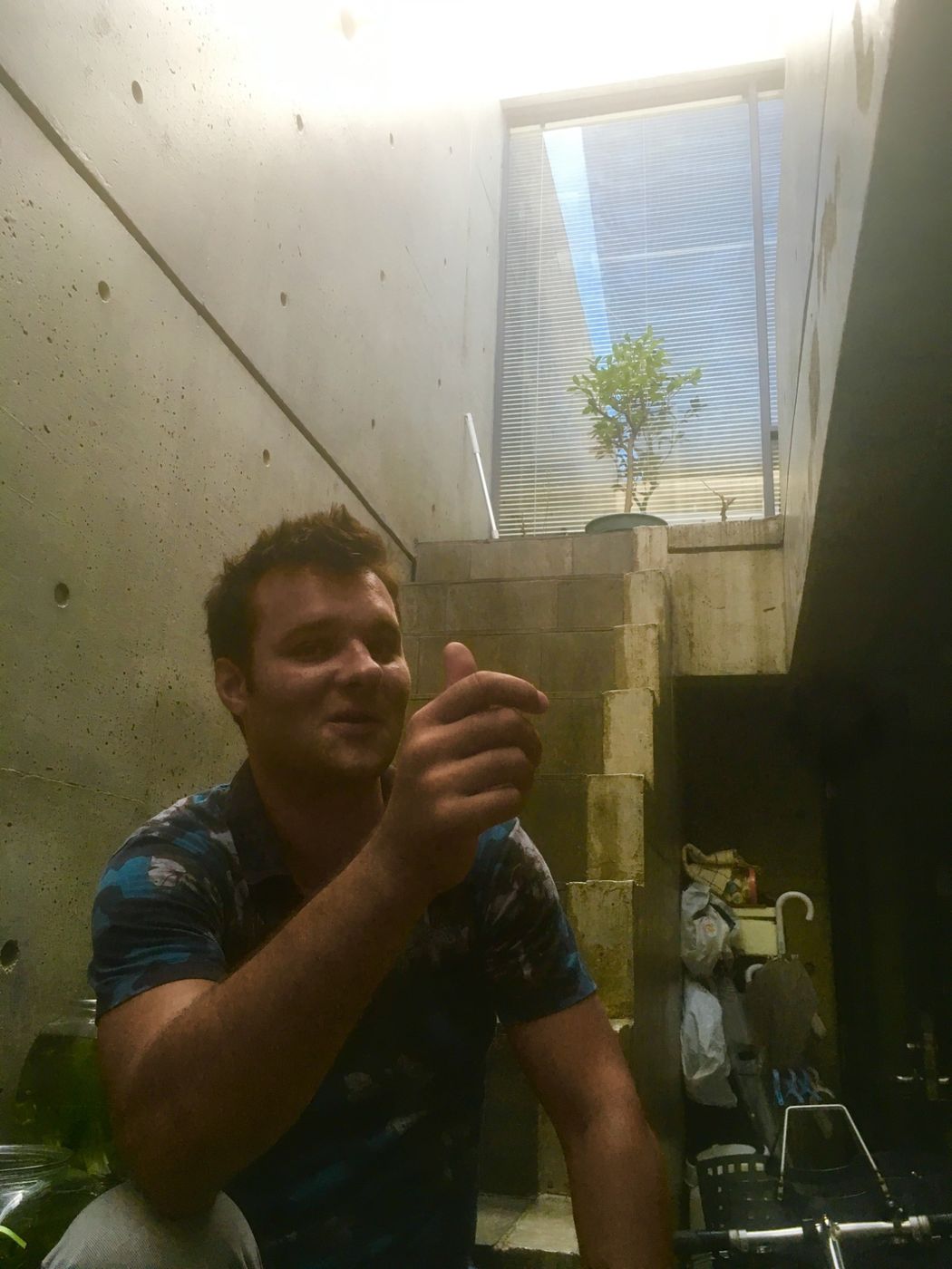 Matteo Gardino seduto dentro la Row House, fra le pareti di cemento: una fessura di luce, la scala di blocchi che sale verso il cortile e un alberello in vaso