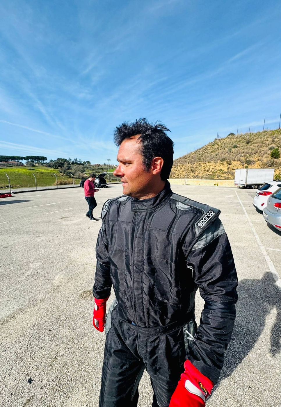 Matteo Gardino in tuta da corsa nera con guanti rossi, in piedi nel paddock di un circuito