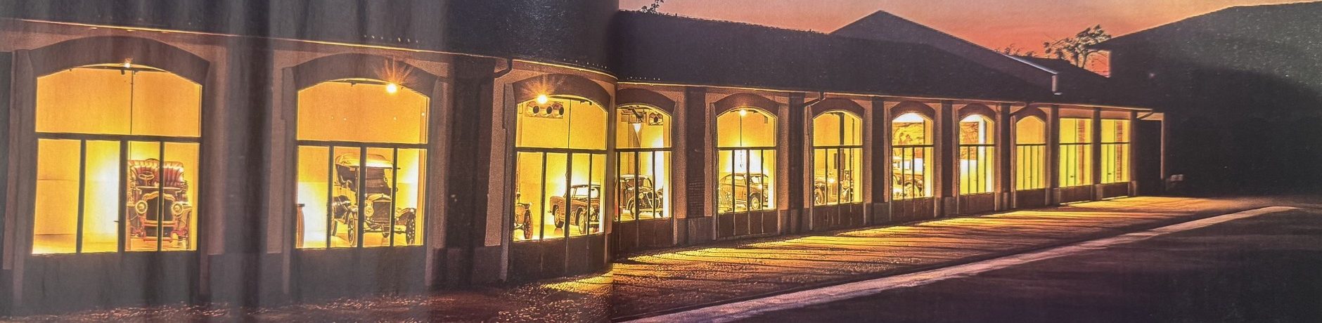 La sala delle automobili al tramonto: una lunga fila di arcate illuminate, con le auto d'epoca dietro le vetrate