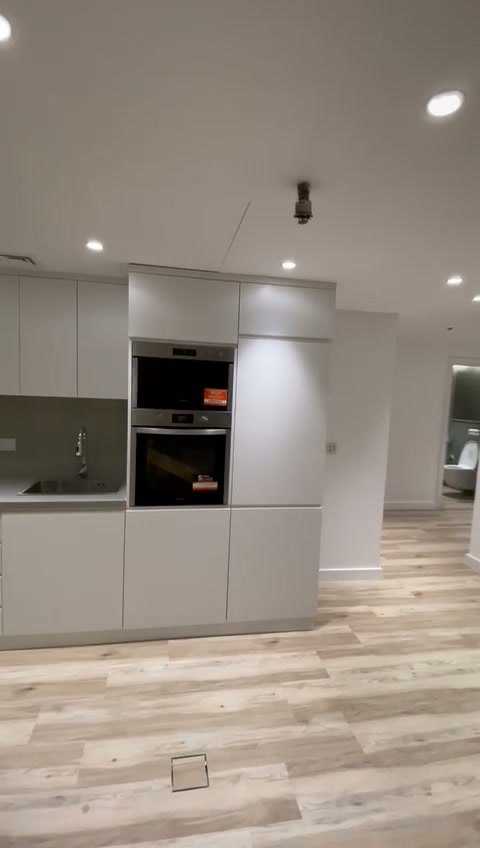 La cucina finita: mobili bianchi a tutta altezza con due forni incassati e il pavimento in parquet lamellare chiaro