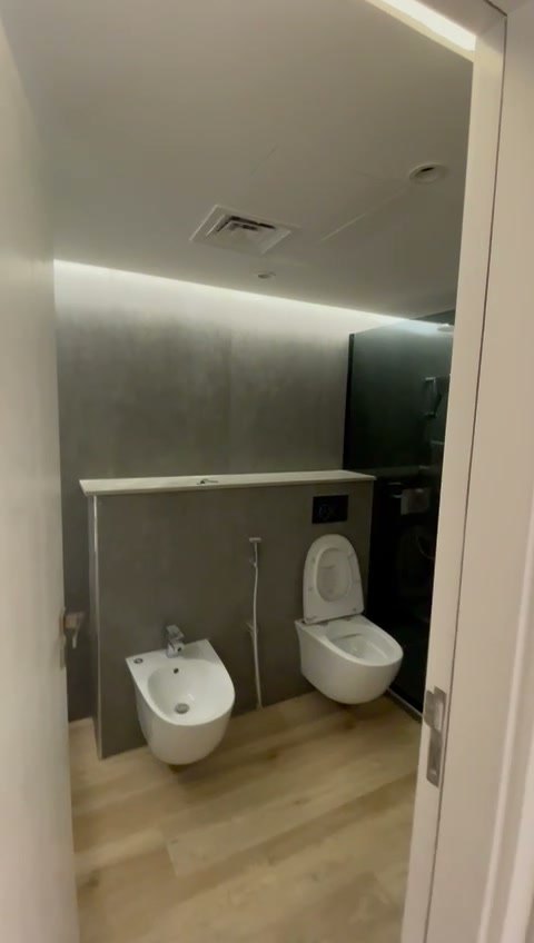 Il vano con wc e bidet sospesi contro la parete rivestita in gres grigio effetto pietra, con la luce radente dall'alto