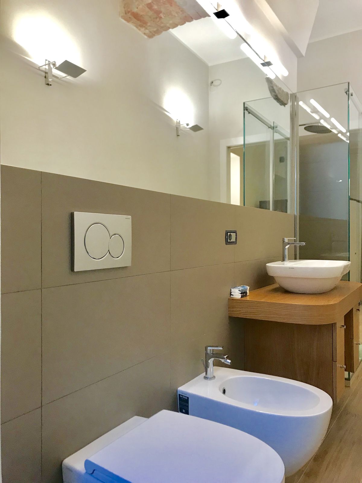 Fotografia del bagno con il box doccia in vetro trasparente, la consolle in rovere a sbalzo, i faretti orientati verso l'alto e la volta di mattoni