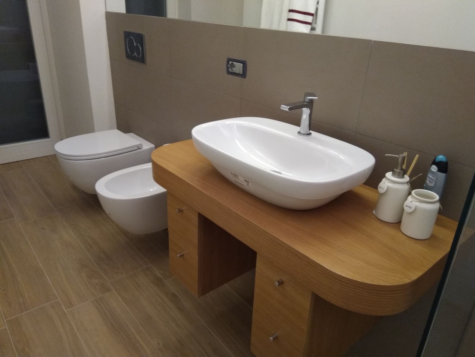 Dettaglio della consolle in rovere: il piano a sbalzo con lo spigolo arrotondato, il lavabo appoggiato, i cassetti sotto, il vaso e il bidet sospesi accanto