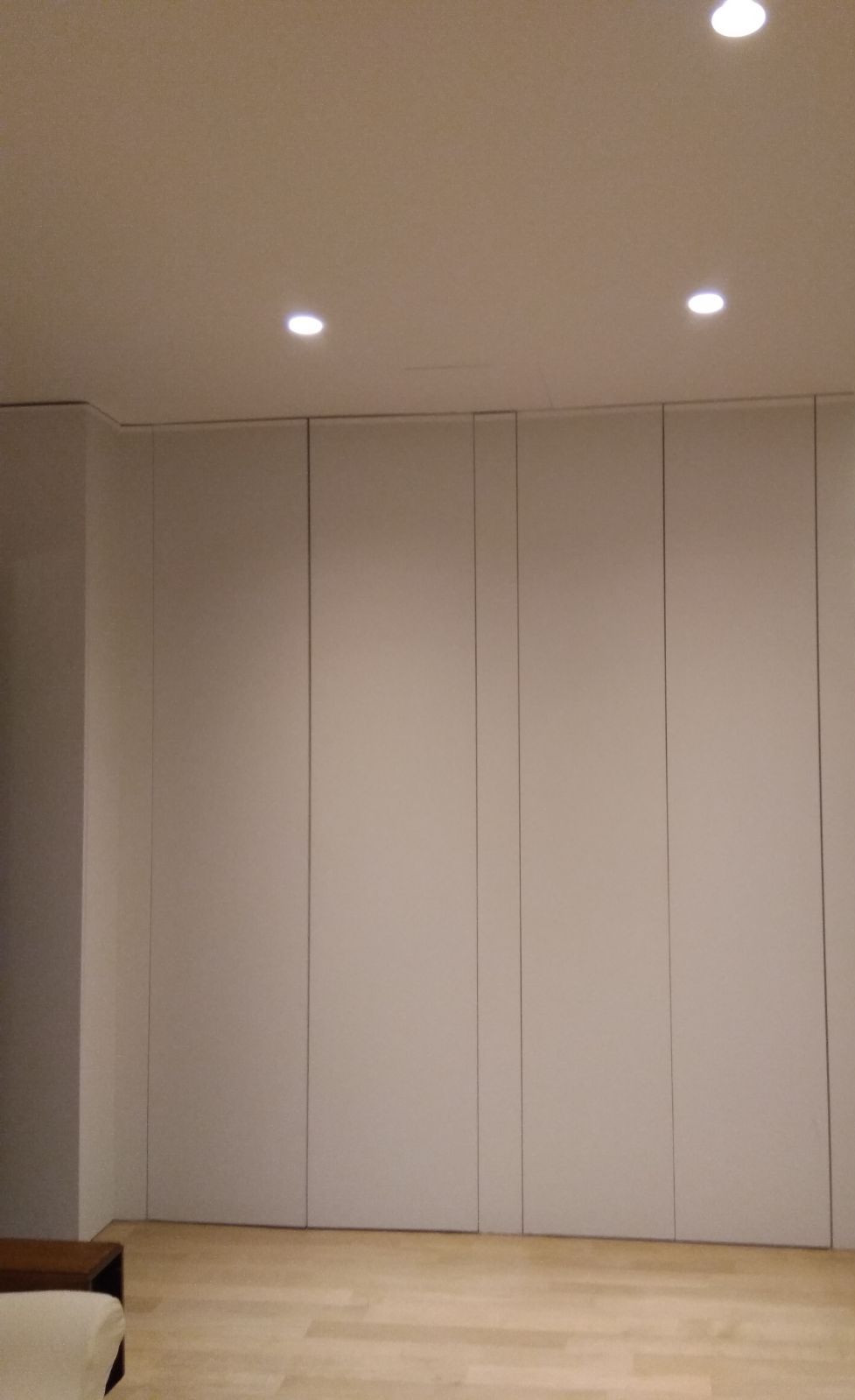 Parete di armadi a tutta altezza con ante a filo muro, senza maniglie, illuminata da faretti a soffitto