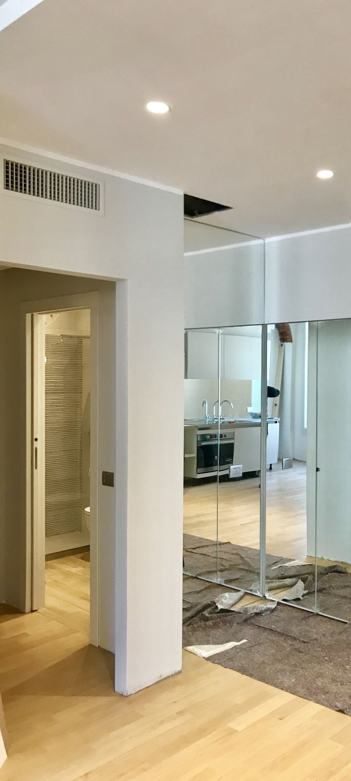 Il disimpegno con la parete a specchio a tutta altezza che riflette la cucina; a sinistra la porta del bagno piccolo; per terra ci sono ancora i teli di protezione del cantiere