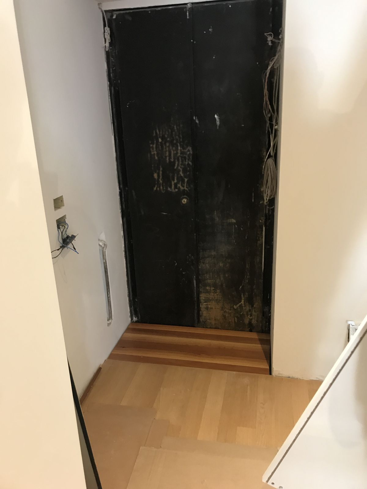 Il vano aperto in fondo al corridoio: una rientranza alta fino al soffitto con il muro vecchio annerito e scrostato, i cavi a vista, il pavimento di legno nuovo che si ferma sul bordo