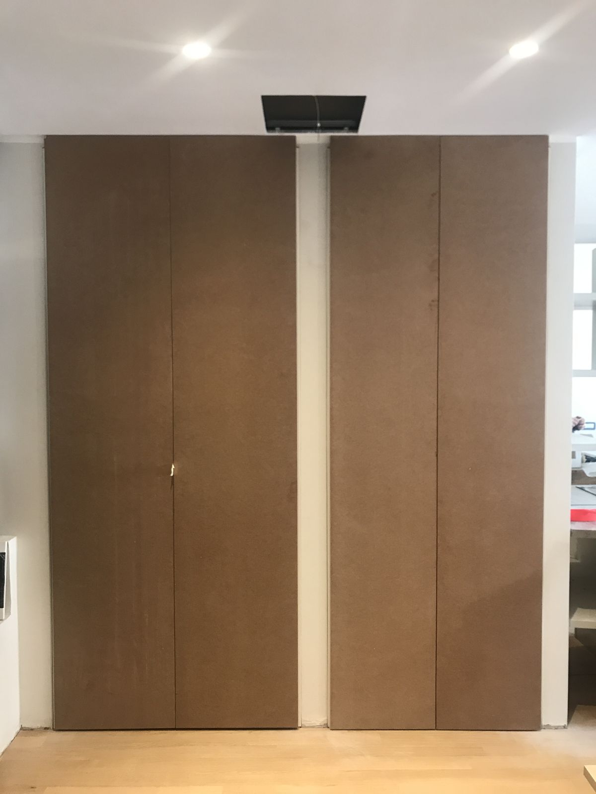 La stessa parete chiusa: due grandi ante a filo dal pavimento al soffitto, senza maniglie, con una sola fuga verticale al centro