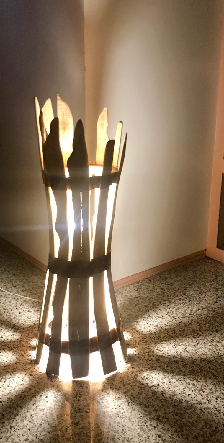 La lampada in ginepro accesa: la luce esce fra le doghe e disegna raggi sul pavimento