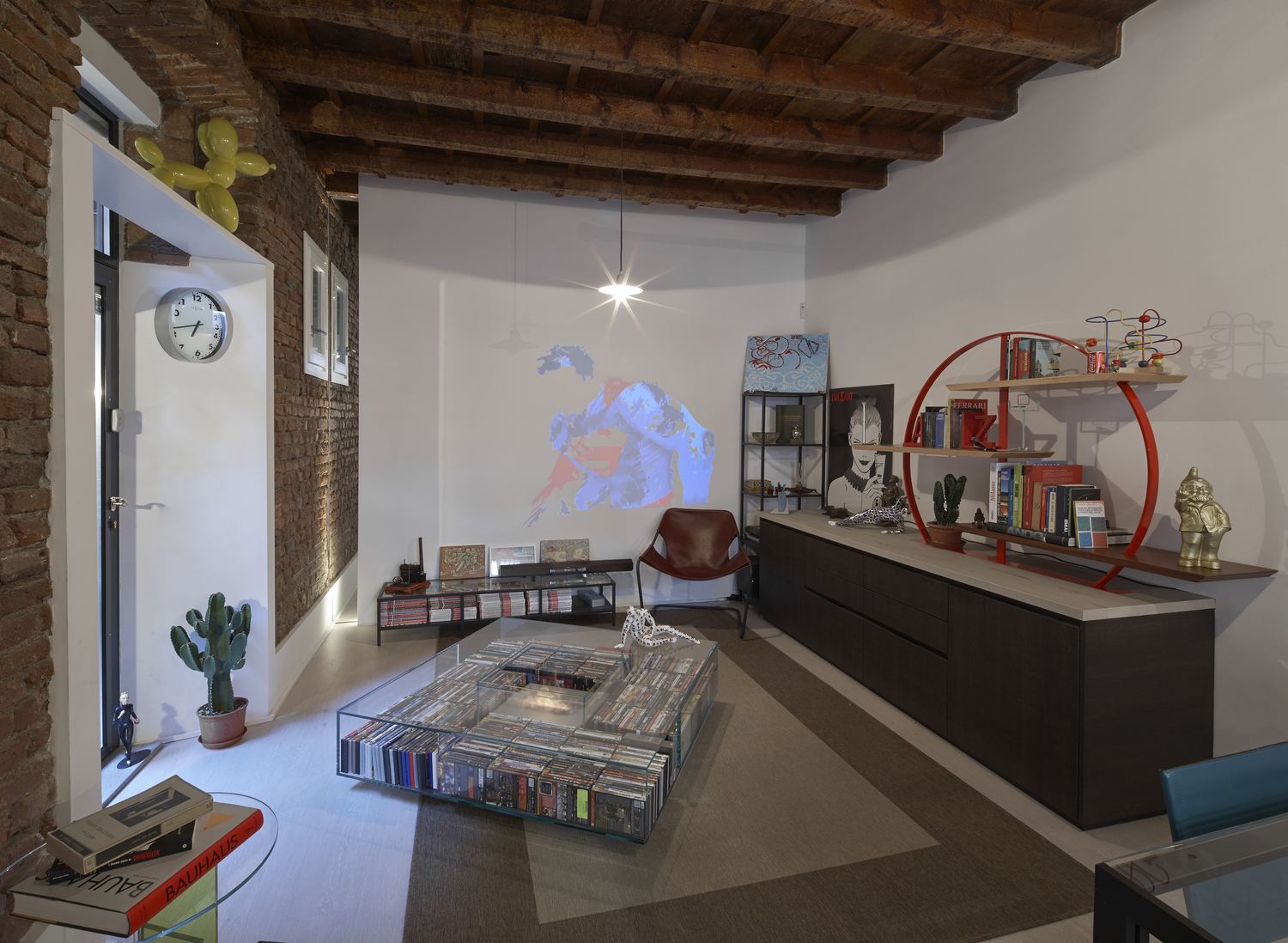 Il soggiorno: muro in mattoni a vista, travi di legno, la libreria circolare rossa e il tavolino di vetro