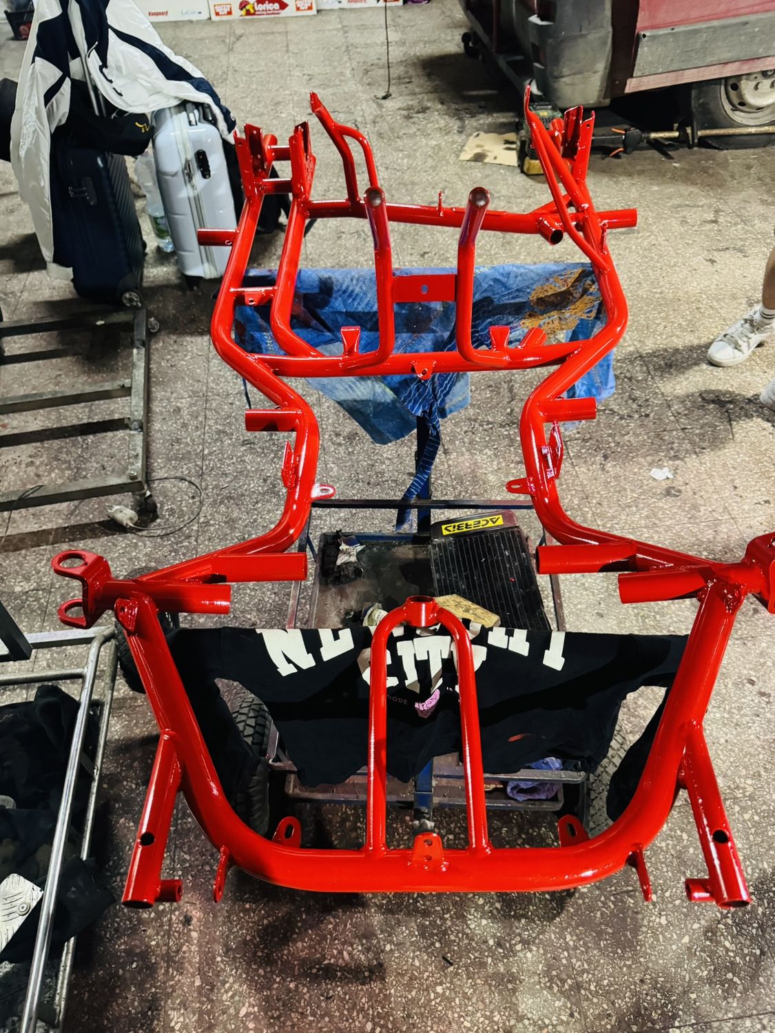 Il telaio del kart nudo, appena verniciato di rosso lucido, appoggiato sul pavimento dell'officina