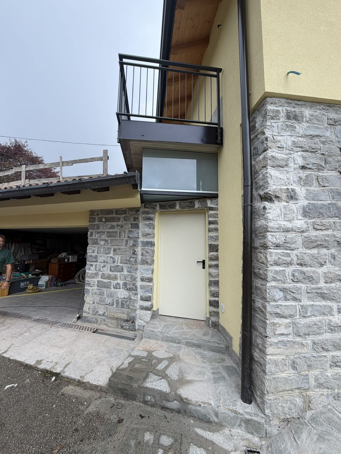Settembre 2026: lo stesso angolo, tutto rivestito in pietra a spacco, con il balcone nuovo in ferro