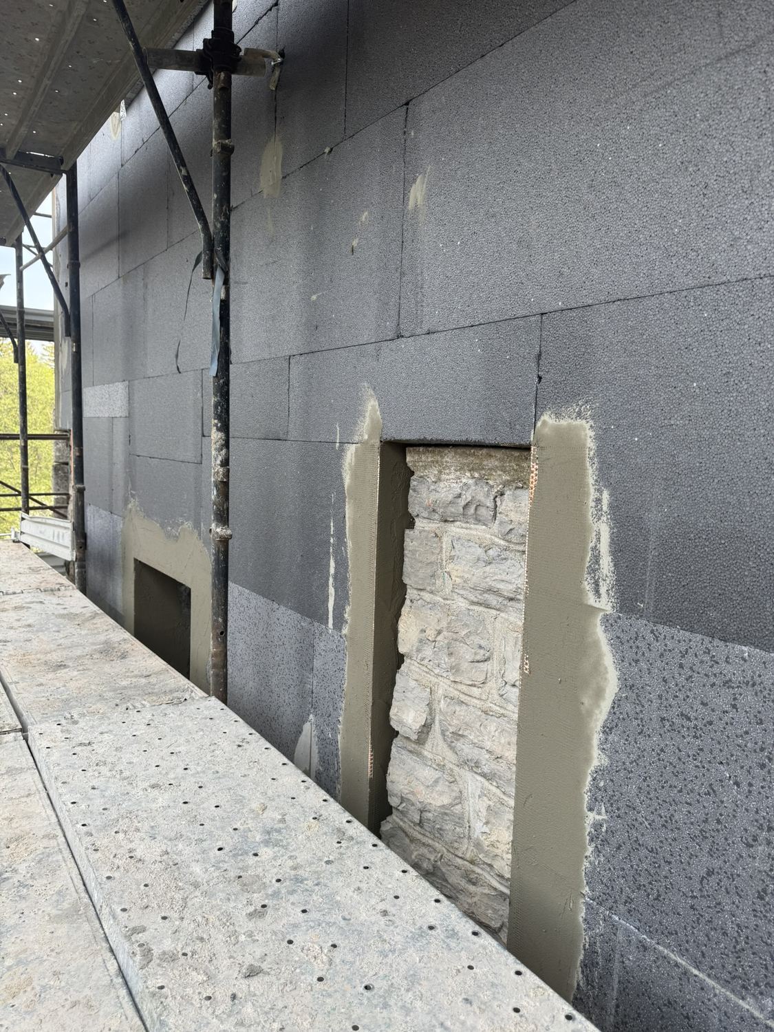 Aprile 2026: il cappotto scuro sul muro, con l'inizio del rivestimento in pietra attorno a un vecchio stipite