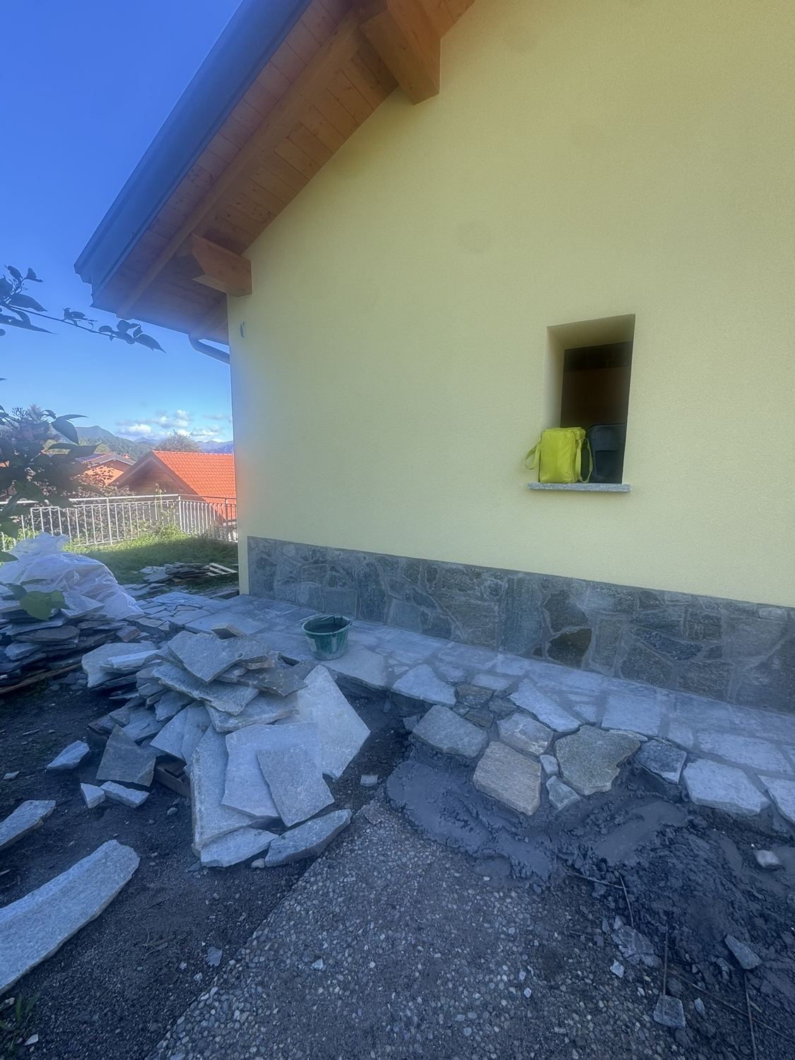 Giugno 2026: la pietra posata sul muro e le lastre irregolari della pavimentazione esterna in corso di posa