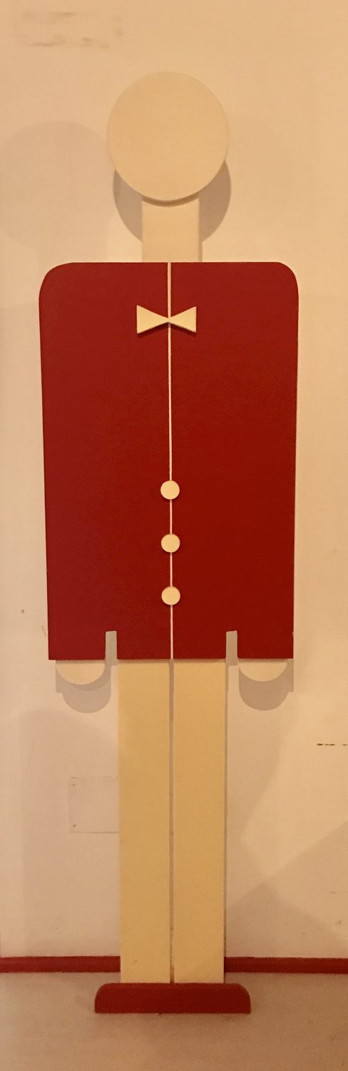 L'Omino fotografato di fronte su fondo neutro: giacca rossa, papillon e bottoni bianchi, pantaloni chiari, base rossa