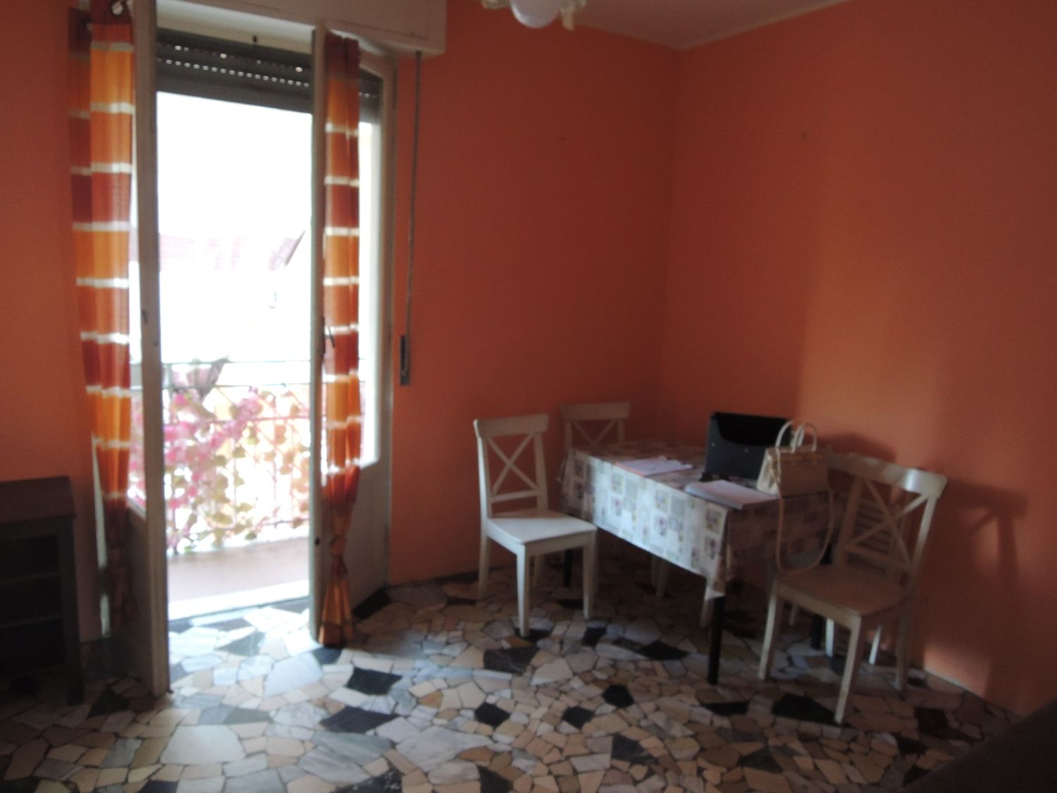 Il soggiorno prima: pareti color salmone, tavolo e sedie, pavimento in graniglia, porta finestra sul balcone