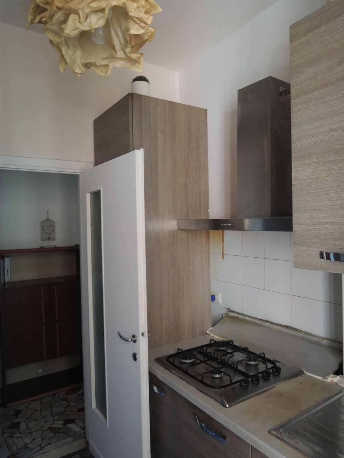 La cucina prima: mobili in laminato chiaro, piastrelle a mezza altezza, cappa e piano cottura
