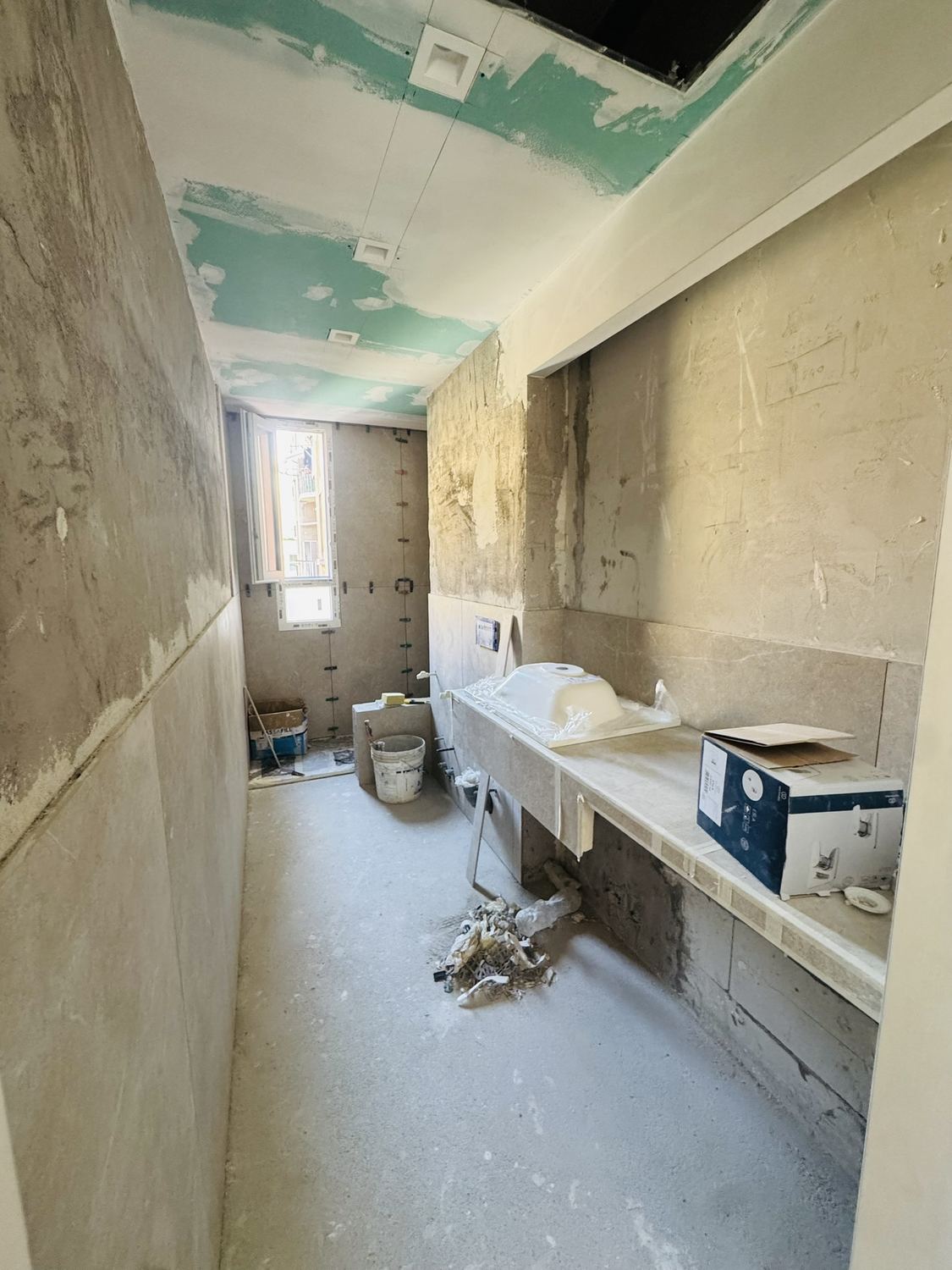 Luglio 2026: le lastre di travertino in opera sulle pareti, il piano del lavabo gi&agrave; montato, il soffitto ancora da chiudere