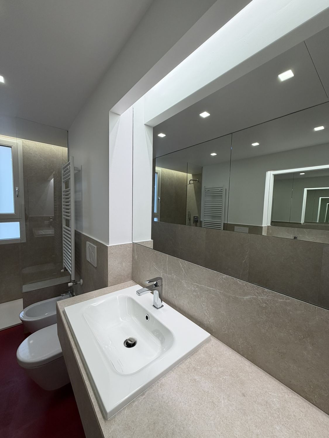 Dettaglio del lavabo: il piano continuo in travertino a sbalzo, il catino appoggiato, lo specchio e la veletta che nasconde la striscia LED