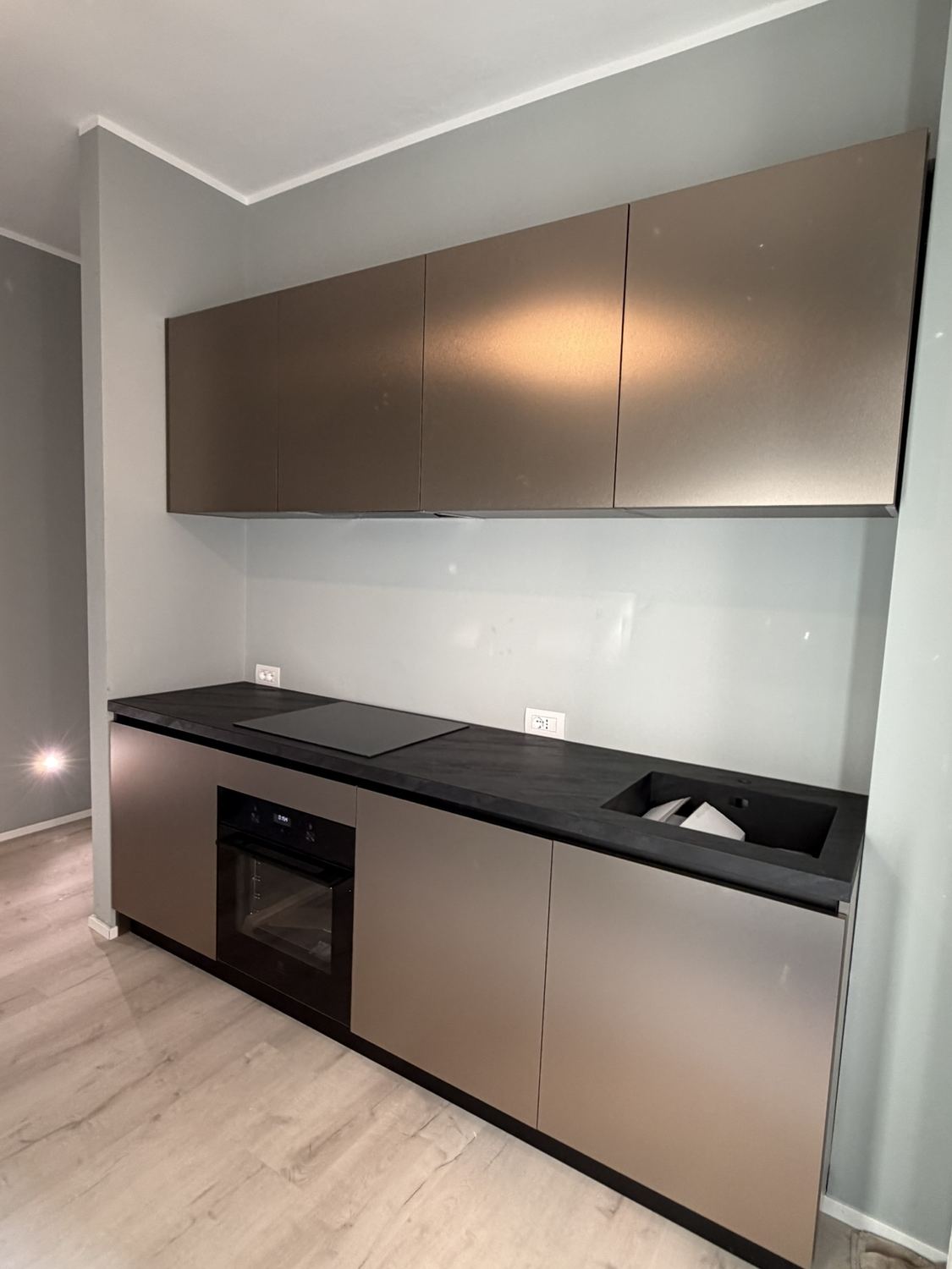 La cucina finita di prospetto: basi e pensili color bronzo, piano nero continuo, forno incassato