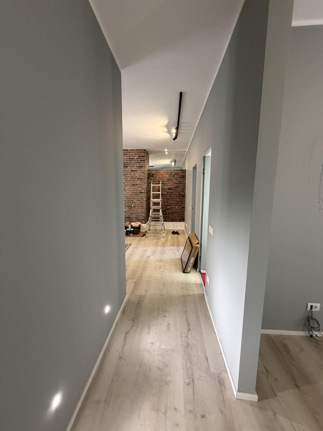 Il corridoio finito: parquet continuo, pareti tortora, il binario con i faretti a soffitto e in fondo la parete di mattone