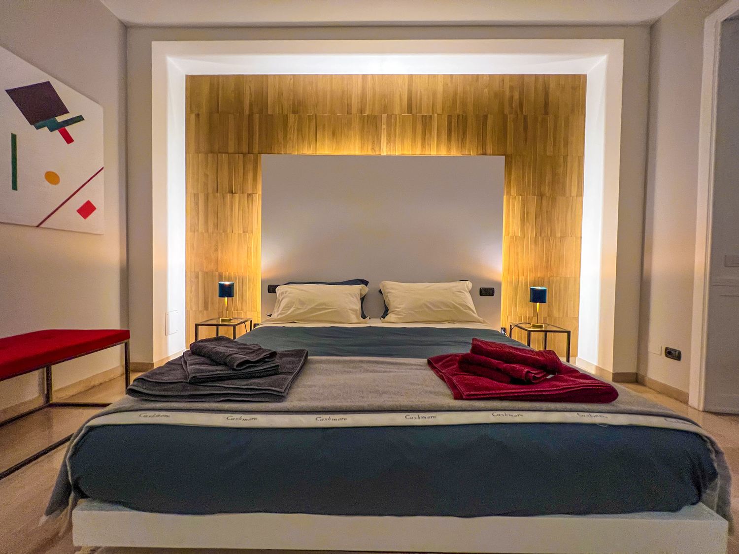 Camera da letto: la testata &egrave; un pannello bianco incassato nella parete in legno, illuminato lungo tutto il perimetro
