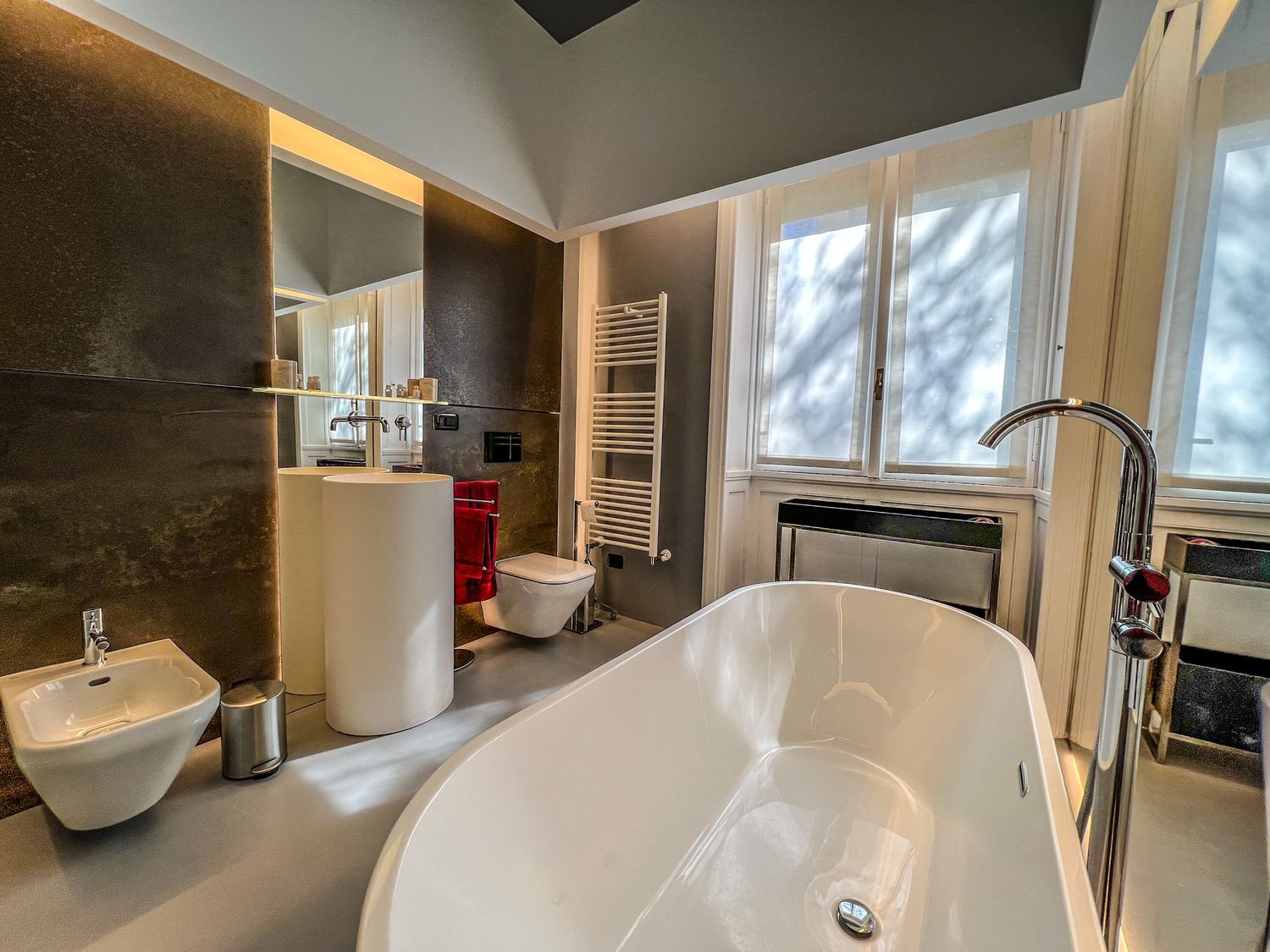Bagno: vasca freestanding, pareti in pietra scura, termoarredo, finestra