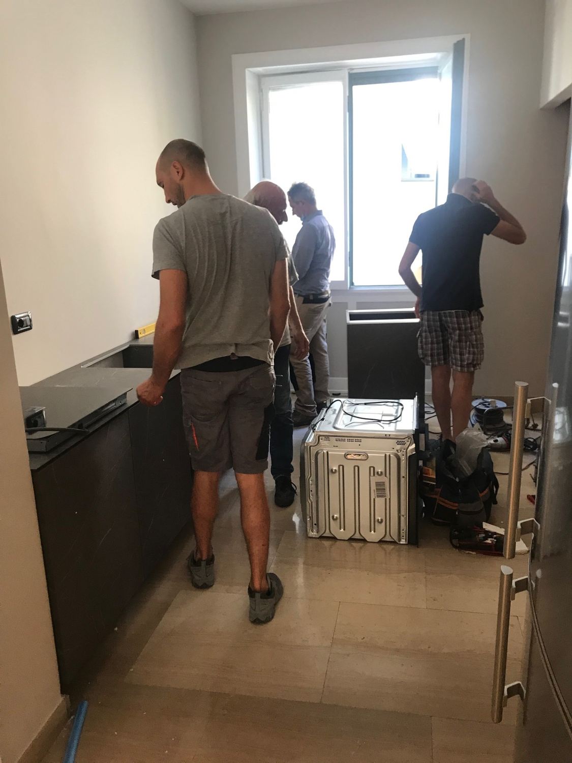 La squadra al lavoro nella cucina: i mobili bassi gi&agrave; in posa con il piano in pietra, il forno ancora appoggiato per terra